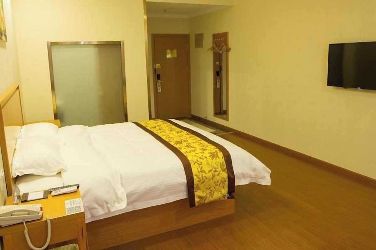 Quarto de hotel com cama, mesa de cabeceira, telefone e televisão na parede.