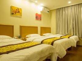 Habitación de hotel con tres camas, cabecera, aire acondicionado de pared y ventana con cortinas.
