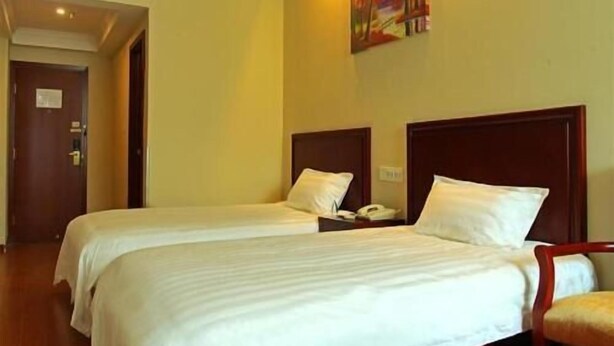 A hotel room with two beds, a painting on the wall, and a door to the left. - Greentree Inn (Tangshan)