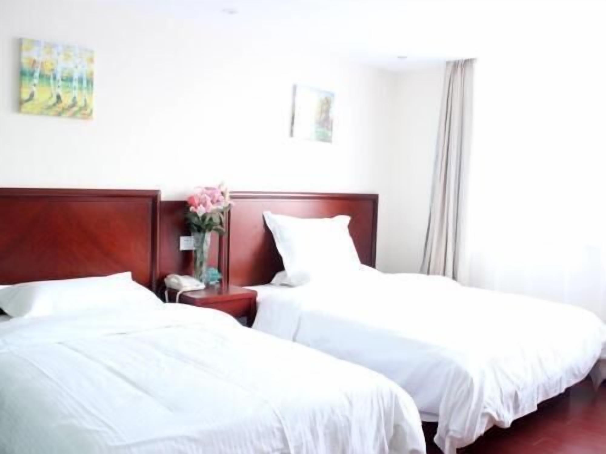 Quarto de hotel com duas camas de solteiro, cabeceira de madeira, mesa de cabeceira com um vaso de flores e um quadro na parede.