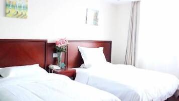 Quarto de hotel com duas camas de solteiro, cabeceira de madeira, mesa de cabeceira com um vaso de flores e um quadro na parede.