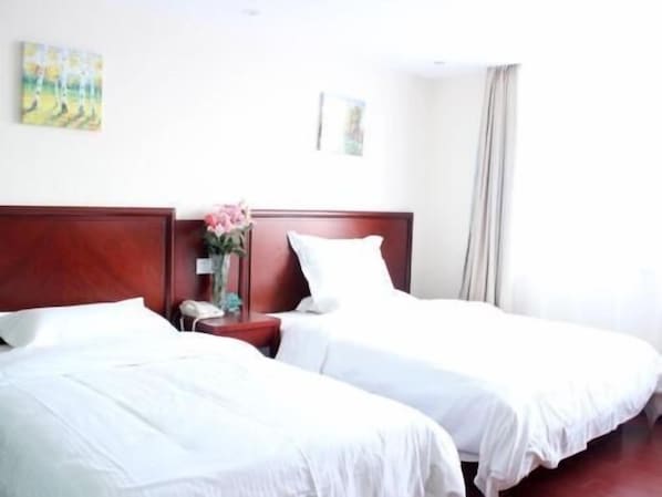 A hotel room with two single beds, a wooden headboard, a bedside table with a vase of flowers, and a painting on the wall.
