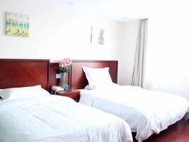 Habitación de hotel con dos camas individuales, cabecera de madera, mesita de noche con un jarrón de flores y un cuadro en la pared.
