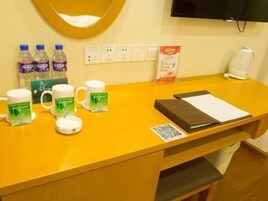 Una recepción con un mostrador amarillo, un televisor montado en la pared, una cafetera y algunas botellas de agua.
