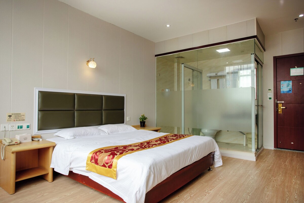 A hotel room with a bed, bedside table, and a glass-enclosed shower area.