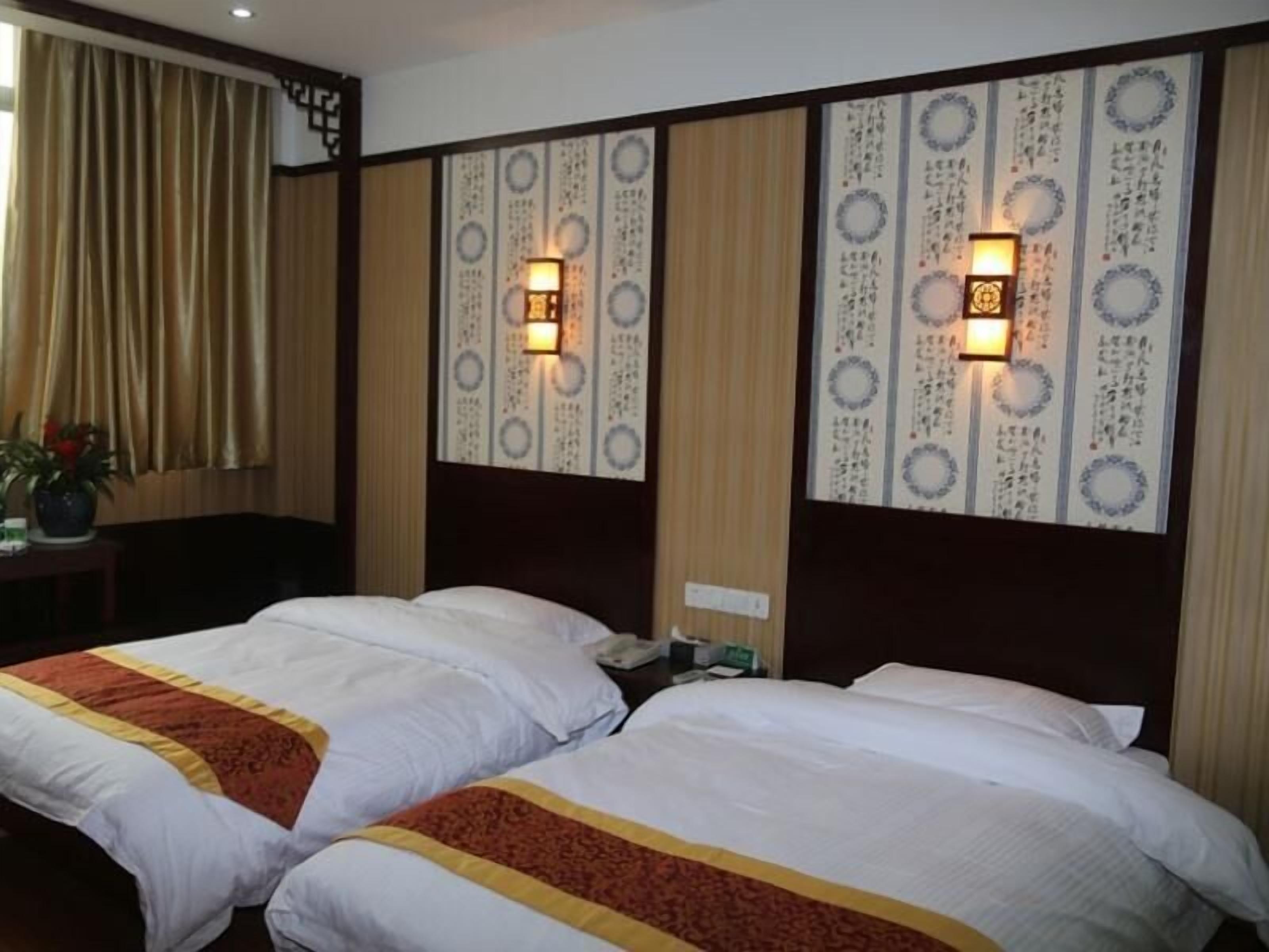 A hotel room with two beds, a desk, a chair, and a potted plant.