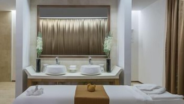 Habitación de hotel con un espejo grande, dos lavamanos, una cama con cubrecama blanco y cabecera de madera.