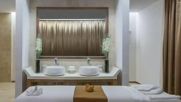 A hotel room with a large mirror, two sinks, a bed with a white bedspread, and a wooden headboard.