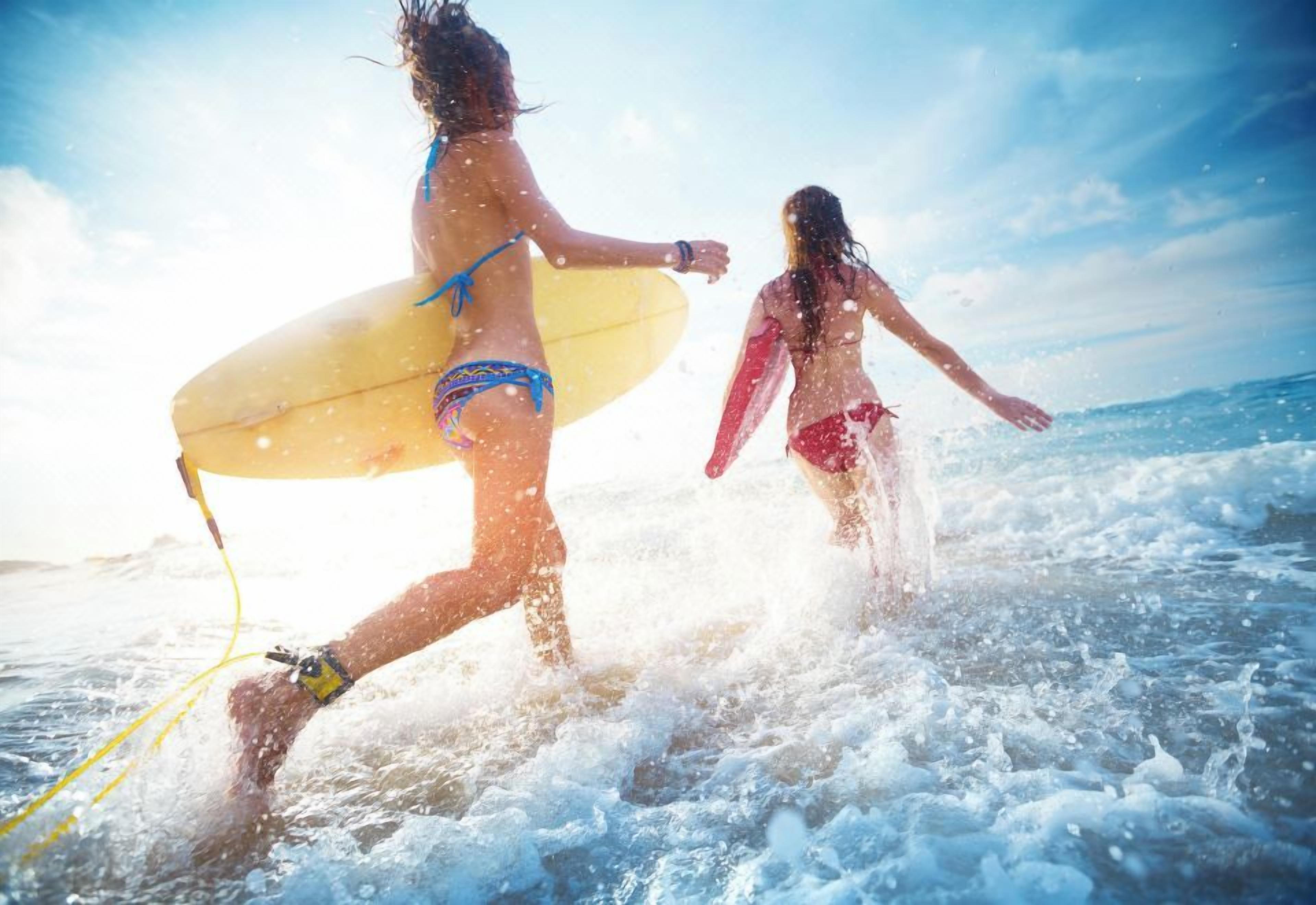Two individuals in a body of water, one carrying a surfboard.