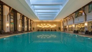 Una piscina interior con techo de tragaluces, sillones de descanso e iluminación ambiental en la pared.