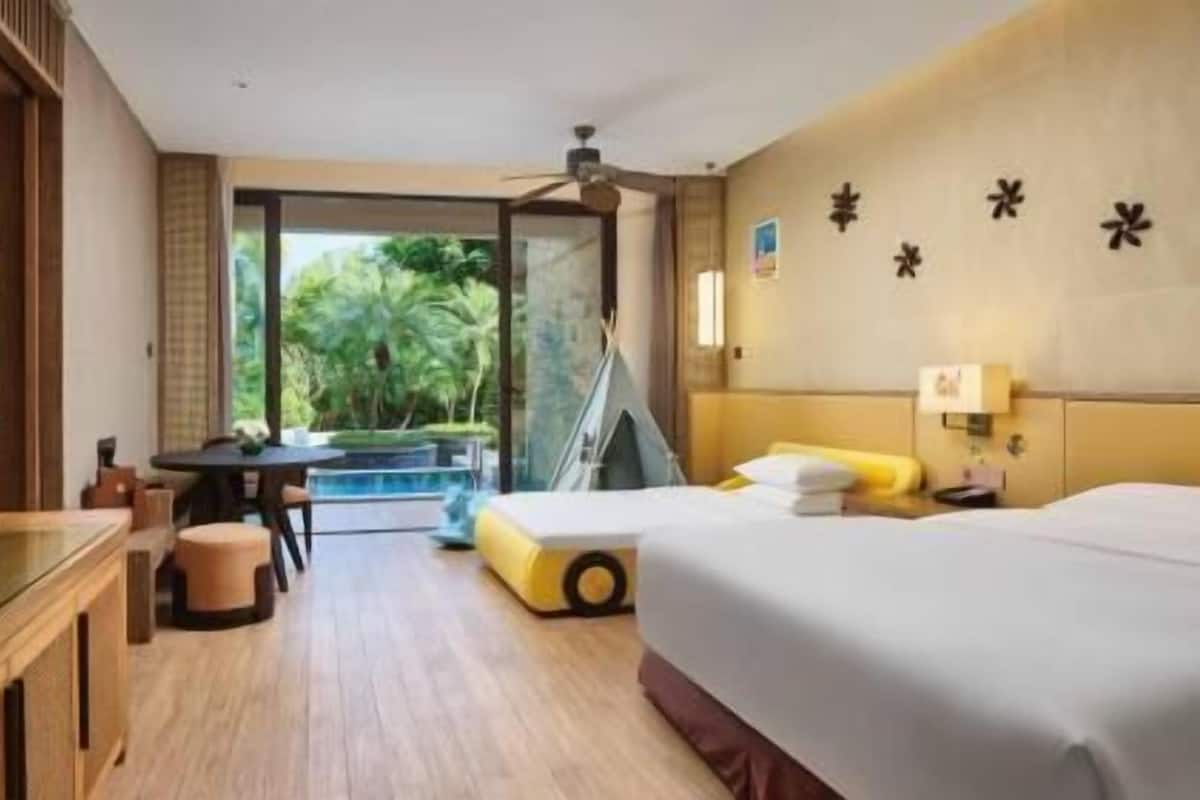 Habitación de hotel con cama, escritorio, silla, televisor y balcón con vista a zonas verdes.