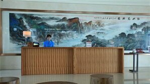 Un mostrador de recepción con una recepcionista, un cuadro tradicional de gran tamaño y una zona de estar con mesas redondas.