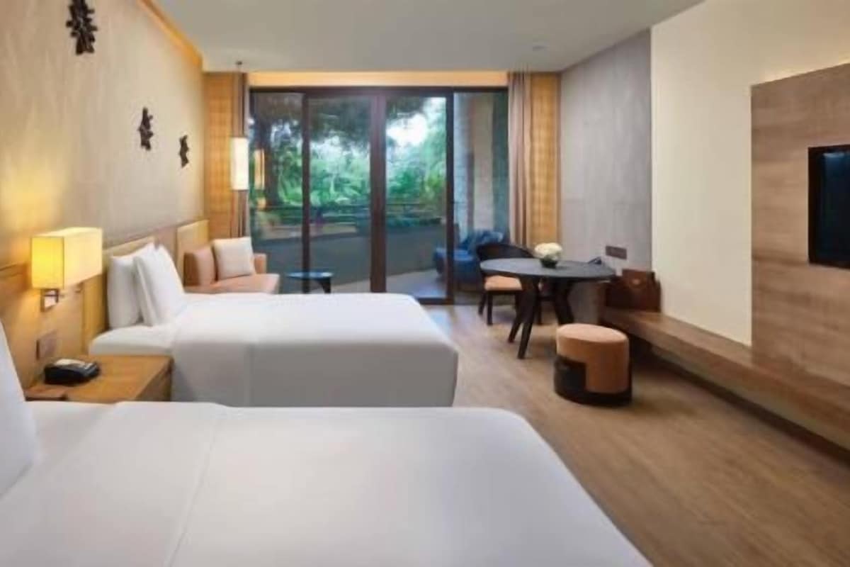 Een hotelkamer met twee bedden, een bureau, een stoel, een televisie en uitzicht op de omgeving.