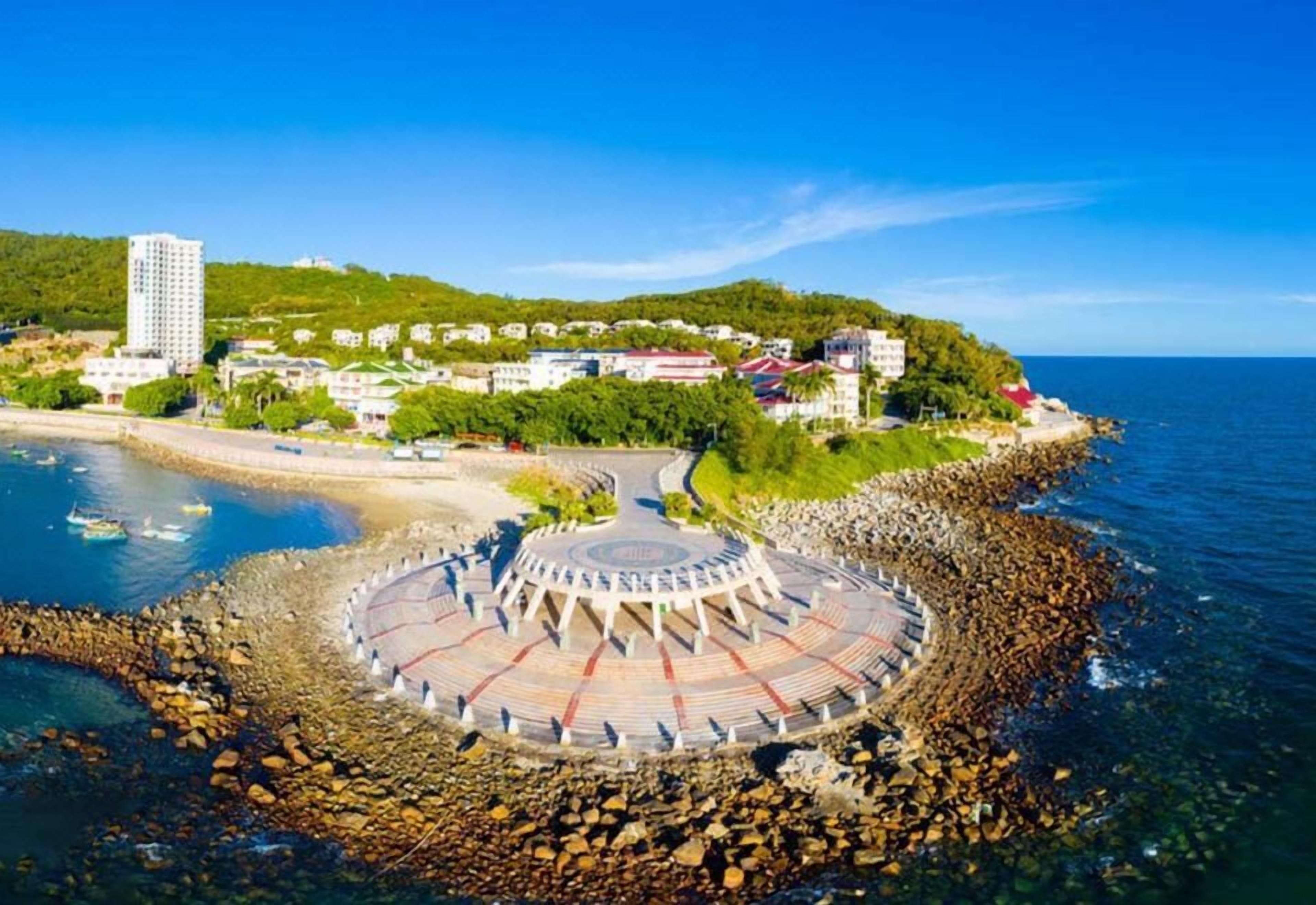 A coastal area with a circular stone structure, buildings, and a clear sky.