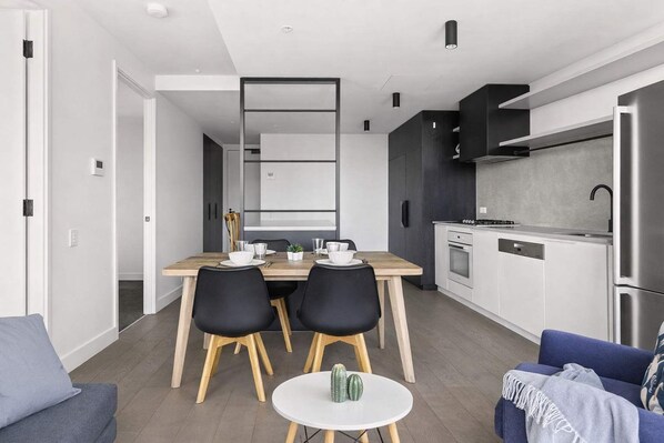 Une cuisine moderne équipée d’un four encastré, d’un réfrigérateur et d’un coin repas avec une table en bois et des chaises noires.