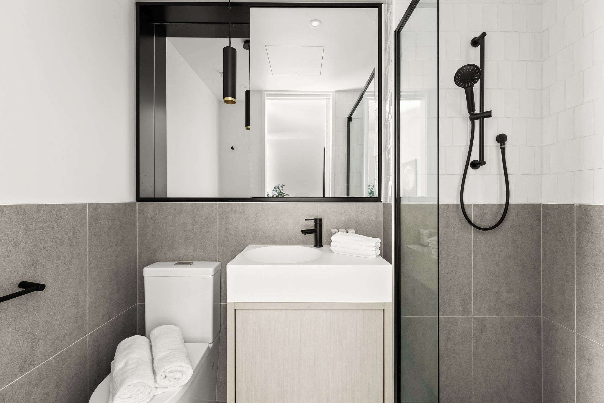 Une salle de bain moderne avec un lavabo blanc, un robinet noir et une douche séparée par une paroi de verre.