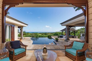 A covered outdoor area with wicker furniture, a glass table, and a view of a pool and ocean. - Spacious 4-Bedroom Ocean View Villa / Infinity Pool & Outdoor Living (Bel Ombre)