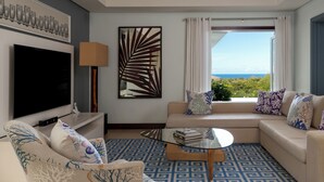 A living room with a flat-screen TV, a sofa with patterned cushions, a coffee table, and a large window with curtains. - Spacious 4-Bedroom Ocean View Villa / Infinity Pool & Outdoor Living (Bel Ombre)