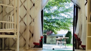 A room with a patterned carpet, a white metal structure, and a view of an outdoor area with a table and chairs. - Ethno Adventure Camp (Almaty)