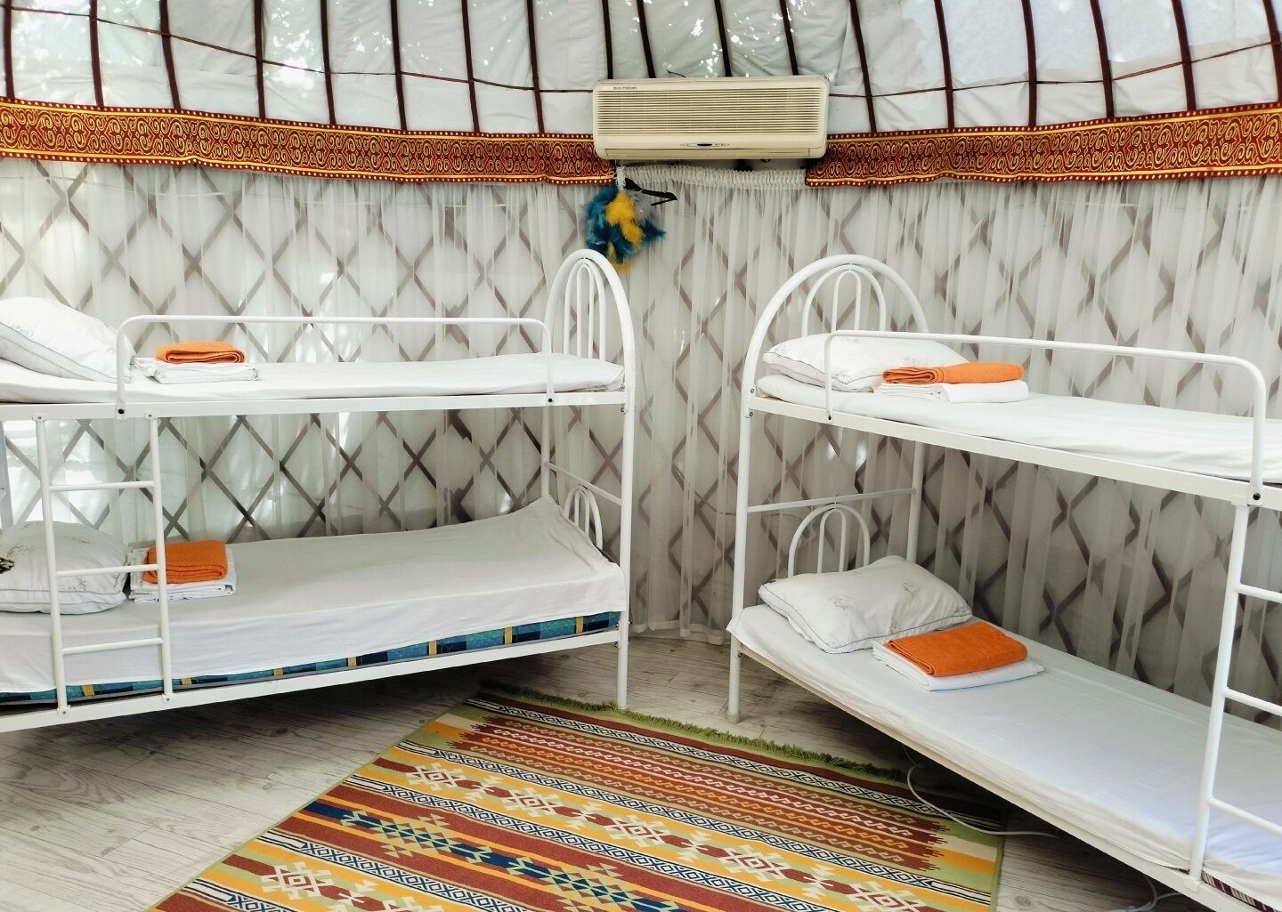 Una habitación con literas, una cortina estampada, un aire acondicionado blanco y una alfombra colorida.