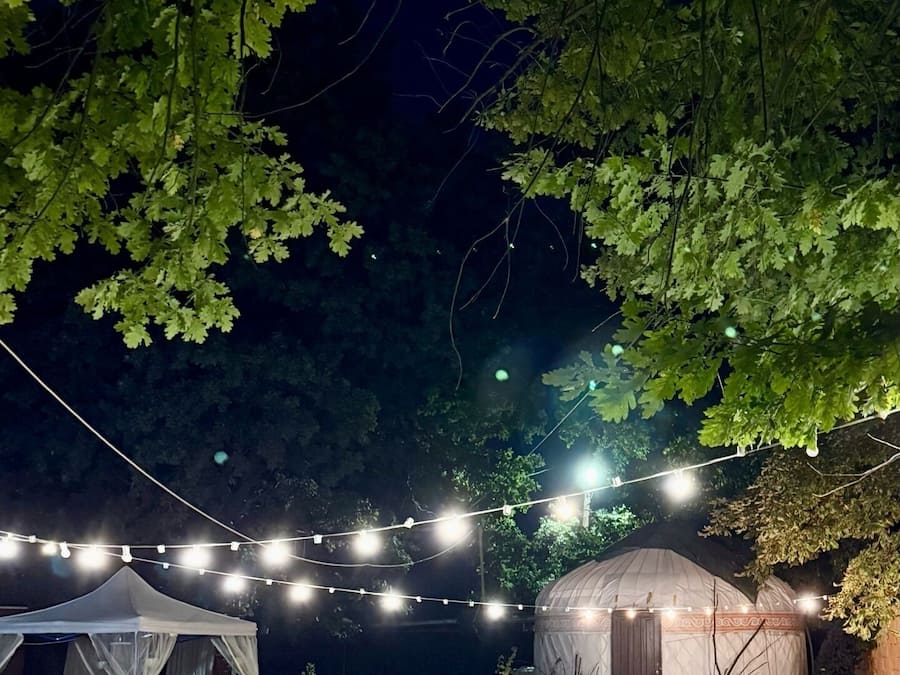 A tented outdoor area with string lights, tables, and benches.