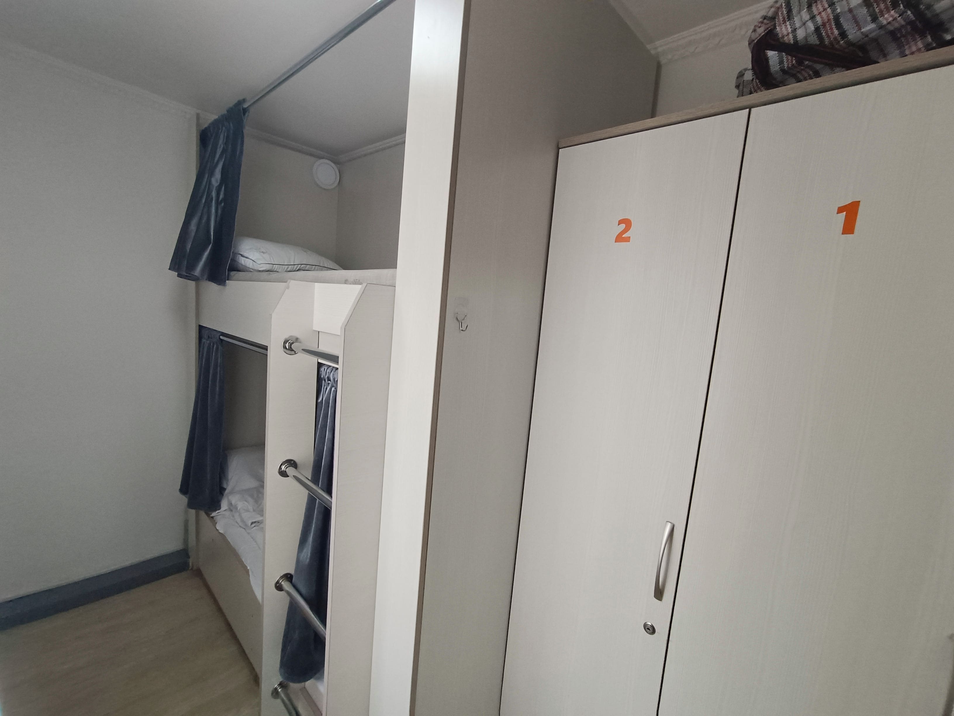 A room with a bunk bed, a wardrobe with numbered doors, and a small round light fixture on the ceiling.