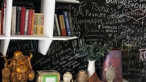 A room with a blackboard wall filled with various writings and drawings, a white bookshelf with books, and decorative items including a Buddha statue and a vase. - Ethno Adventure Camp (Almaty)
