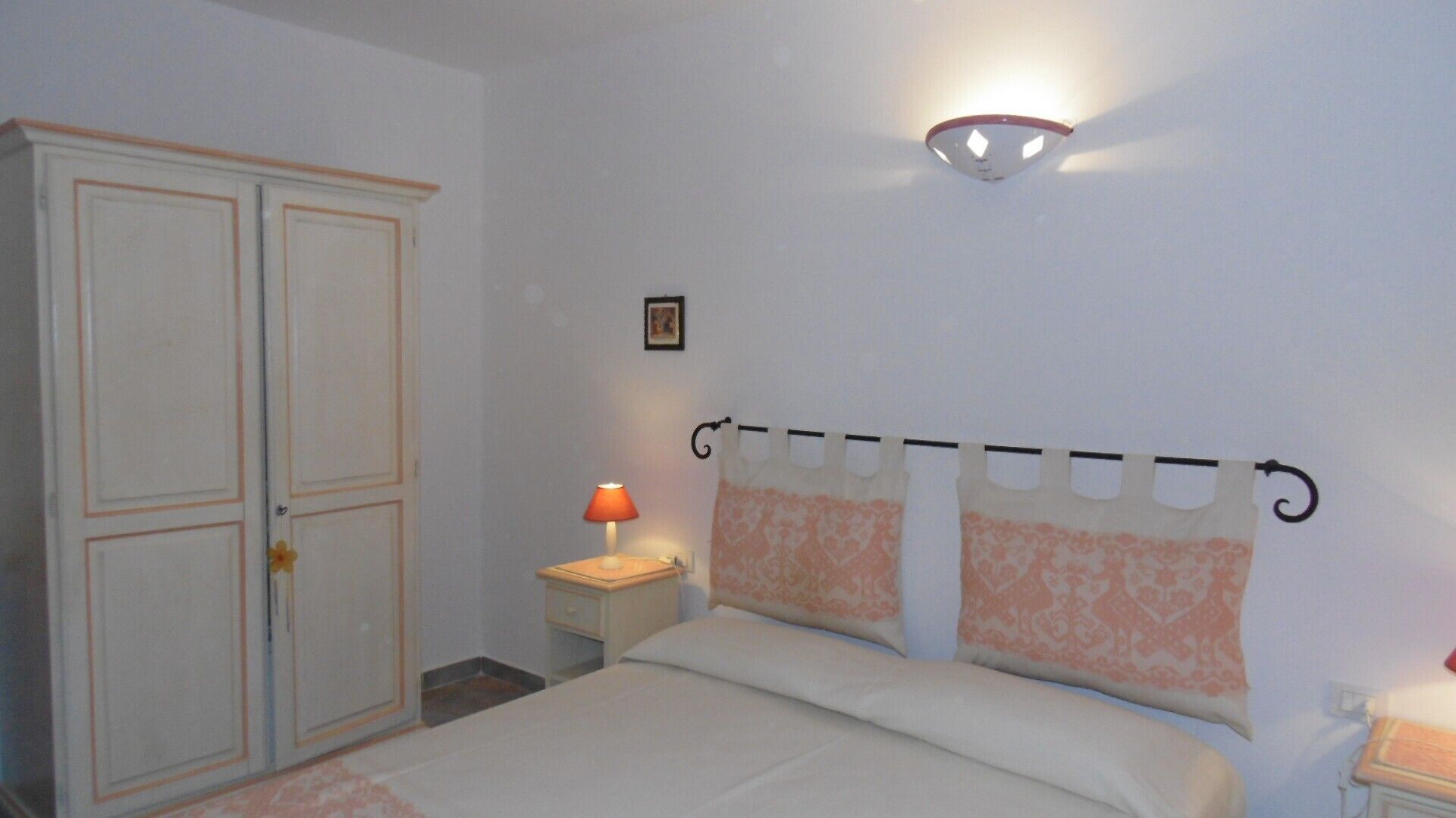 Ein Schlafzimmer mit einem Bett, einem Nachttisch, einer Lampe, einem Kleiderschrank und einer Wandleuchte.