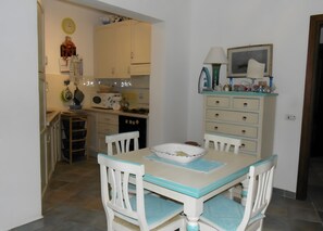 Uma área de refeições com mesa e cadeiras, uma cozinha ao fundo e um banquinho pequeno.