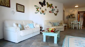 Uma sala de estar com dois sofás brancos, uma mesa de centro e uma área de jantar com uma mesa e cadeiras.