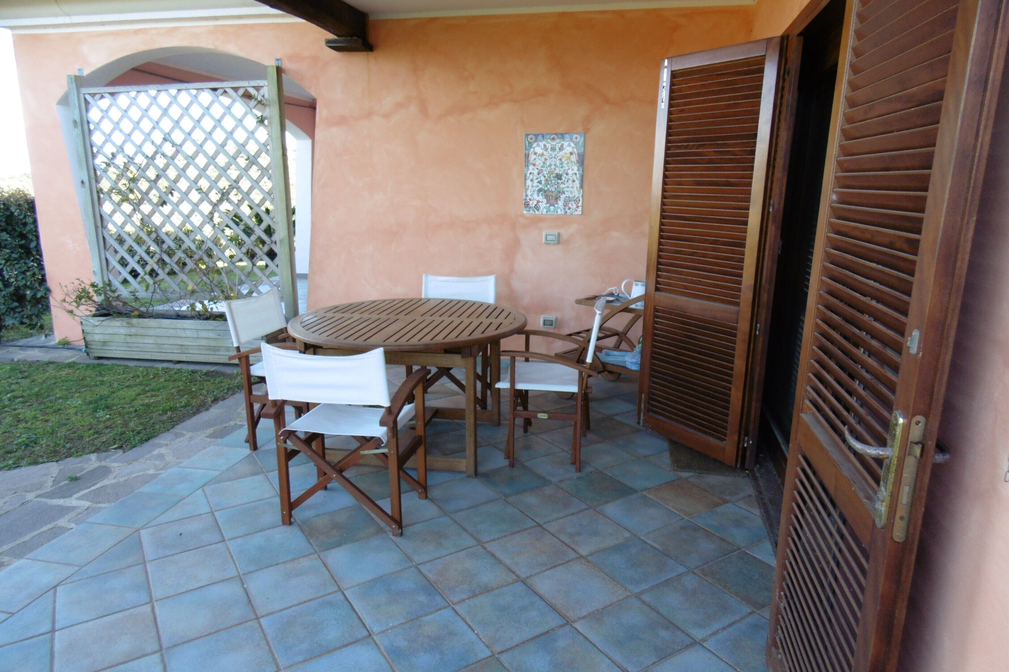 An outdoor patio with a round wooden table and chairs, a small white chair, a wooden door, and a lattice fence.