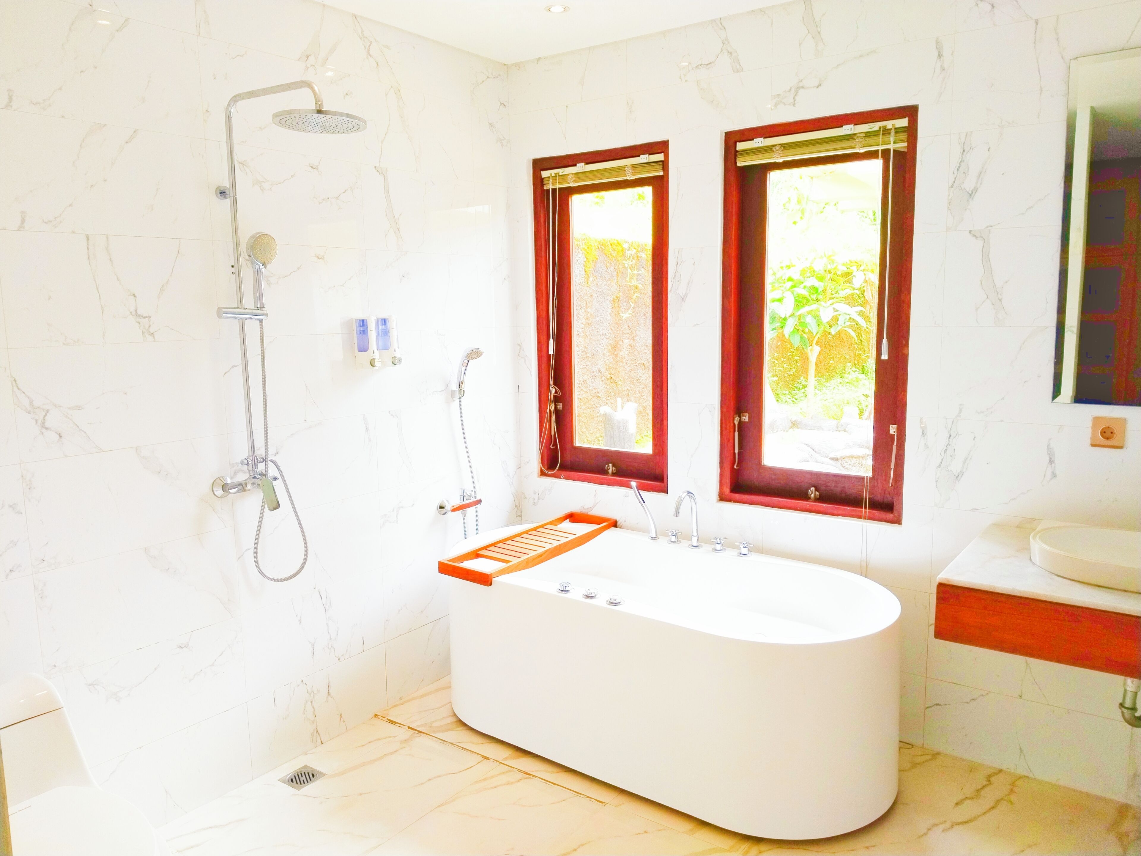 A modern bathroom with a freestanding bathtub, a showerhead, and two windows with red frames.