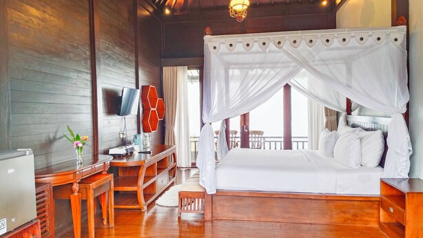 A wooden room with a bed, a desk, a TV, and a view of the outside. - Merlyn Meadows Retreat (Munduk)