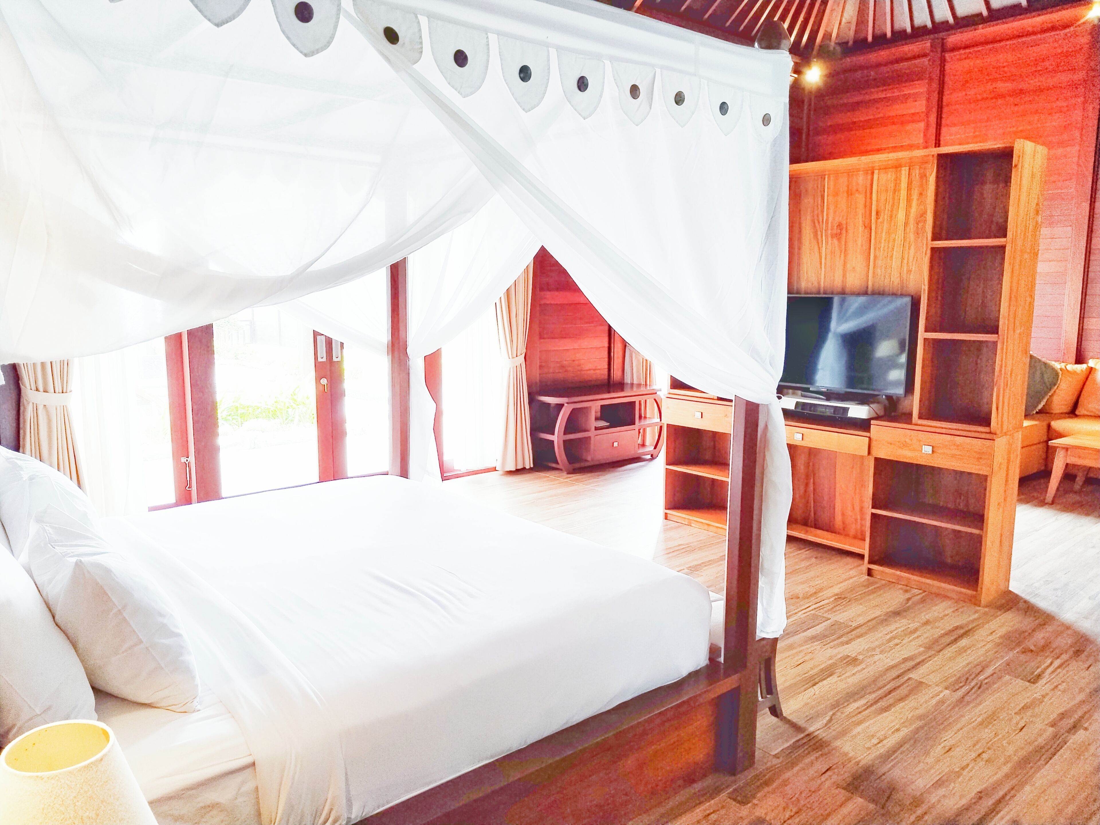 A bedroom with a canopy bed, wooden furniture, a television, and a view of the outdoors.