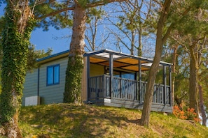 A cabin with a wooden deck, surrounded by trees and greenery.