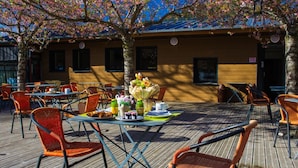 Un café en plein air avec des tables et des chaises, une composition florale et un bâtiment en arrière-plan.