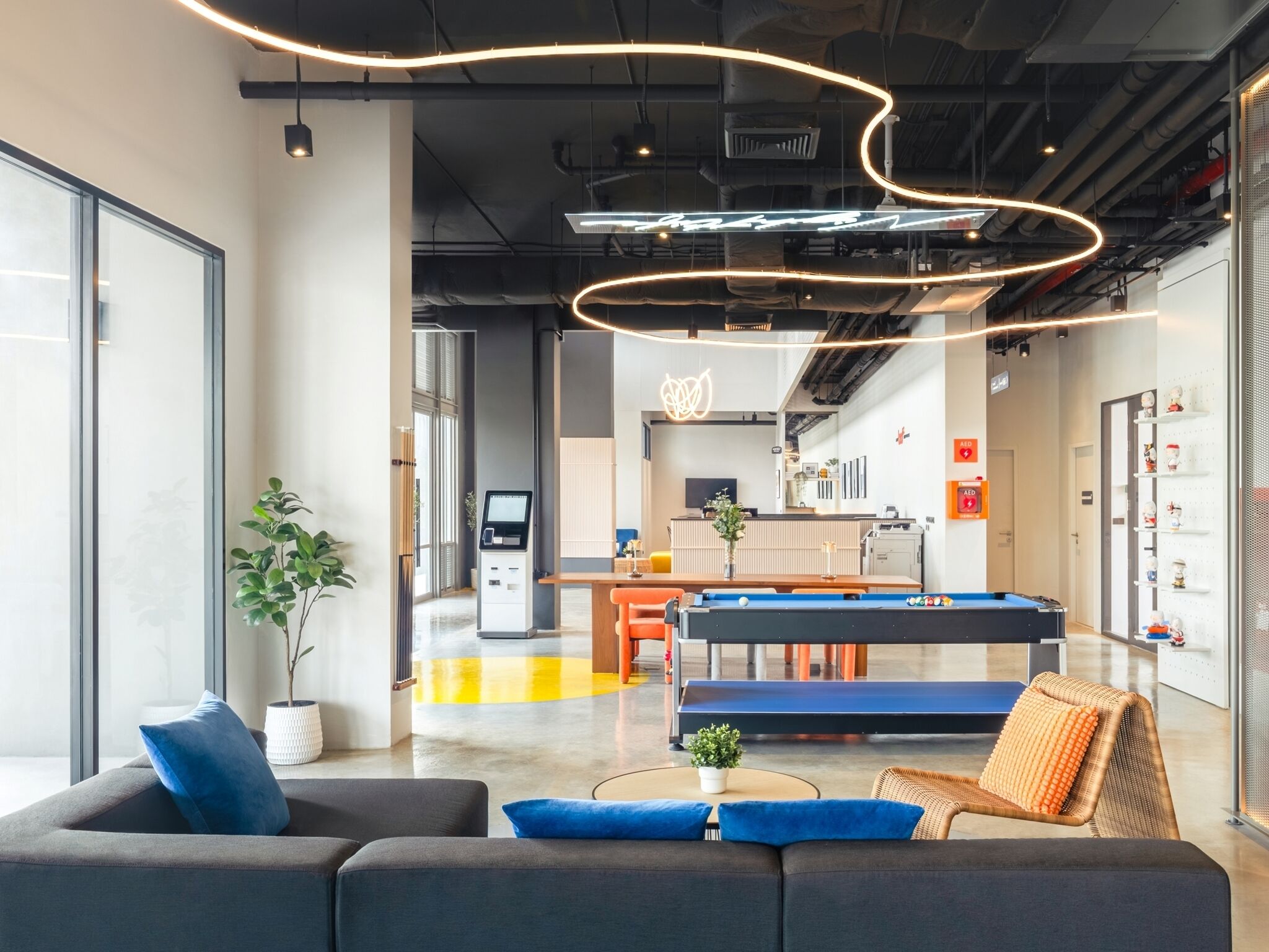 A modern indoor space with a pool table, seating area, and a vending machine.