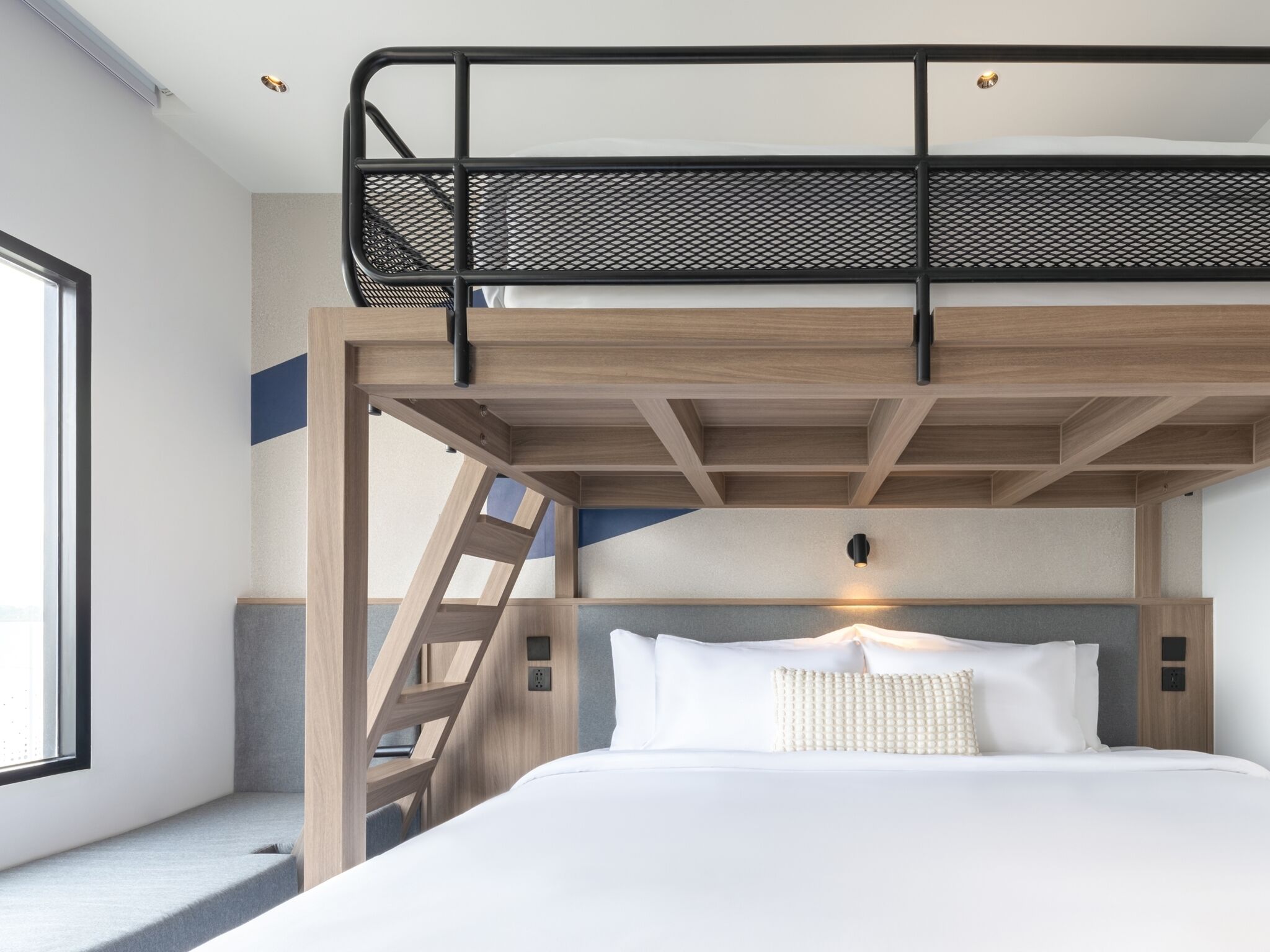 Una cama litera con escalera, una mesita de noche y una lámpara de pared.