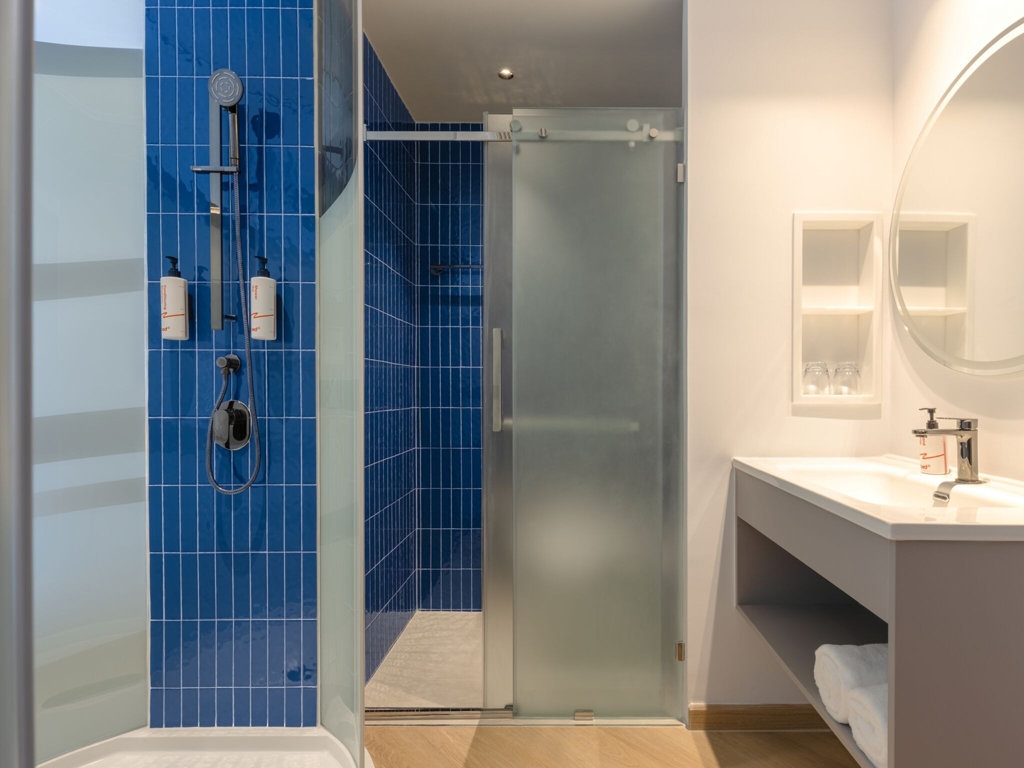 A modern bathroom with a glass shower enclosure, a white sink, and a mirror.