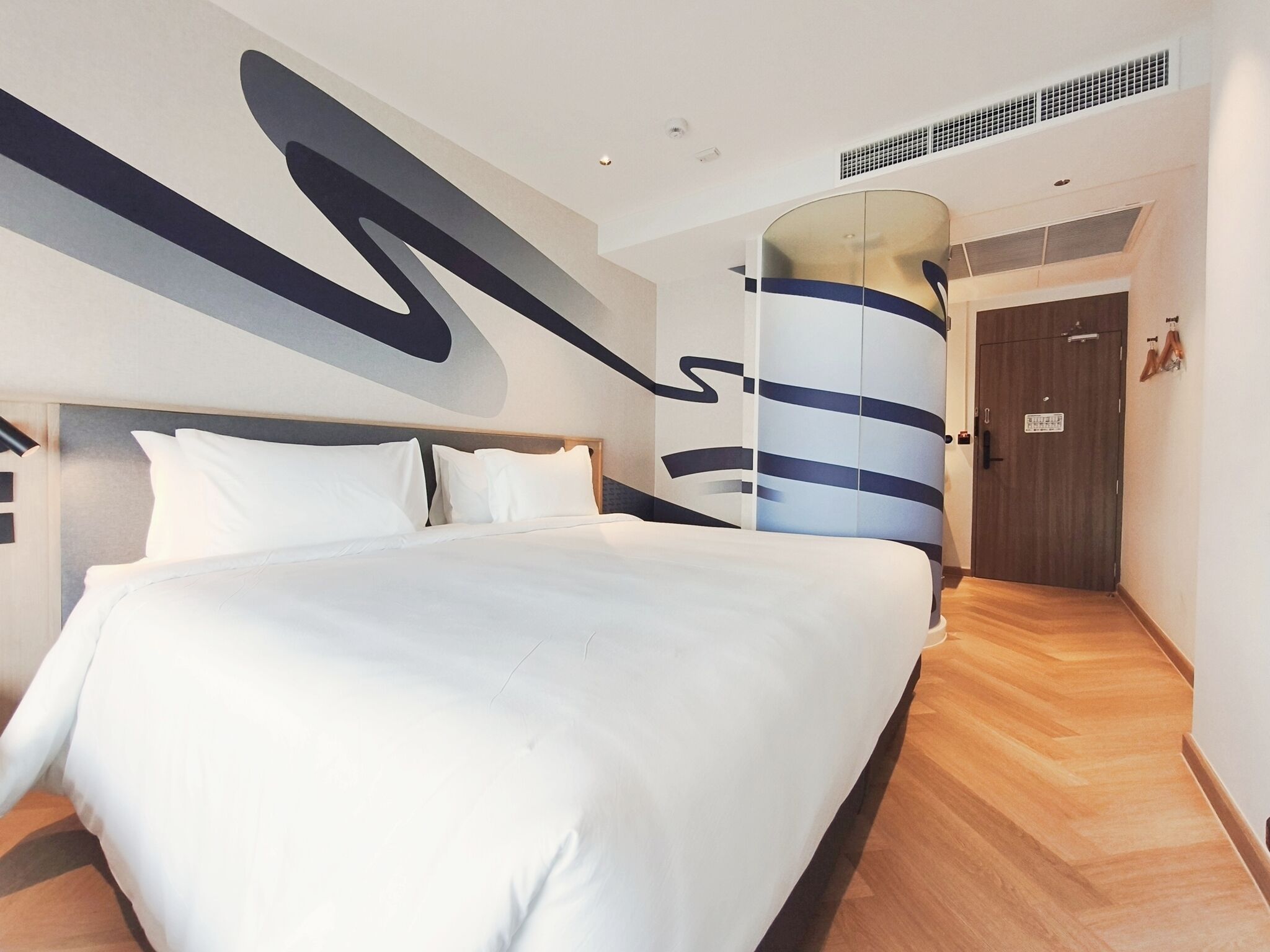 A modern hotel room with a large bed, a wooden floor, and a distinctive wall art piece.