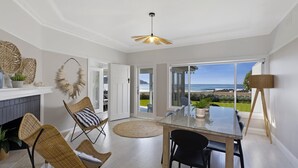 Um quarto espaçoso com uma mesa de vidro, cadeiras de vime, lareira e vista para o oceano.