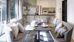 Un salon moderne comprenant un ensemble de canapés, une table basse et une table à manger avec des chaises. On aperçoit une cuisine en arrière-plan, avec des meubles blancs et un four à micro-ondes.