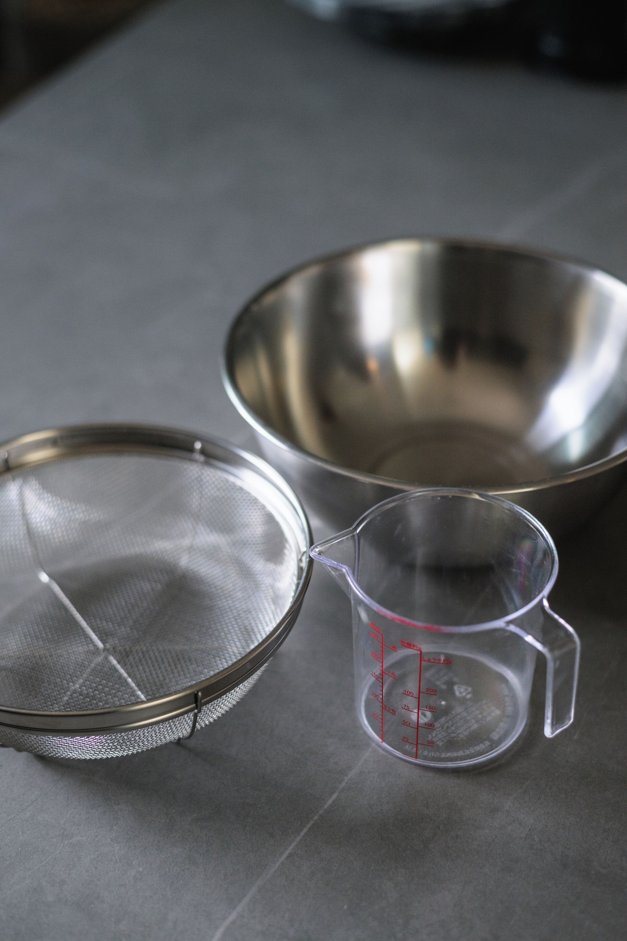 A kitchen with a stainless steel bowl, a measuring cup, and a strainer.