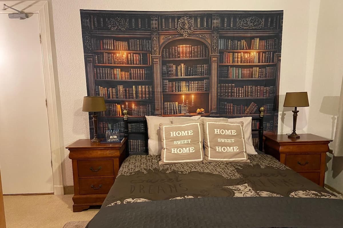 A bedroom with a large bookshelf, two bedside tables with lamps, and decorative pillows.