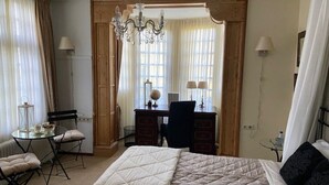 Ett hotellrum med en säng, ett skrivbord, en stol och en kristallkrona.