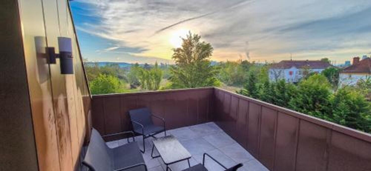 Un balcon donnant sur un paysage urbain, une table et deux chaises.