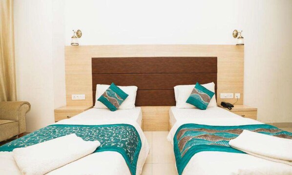 Una habitación de hotel con dos camas, cabecera de madera, mesitas de noche con lámparas y una silla.