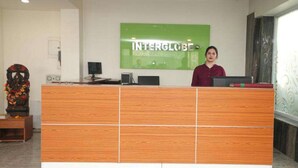 A reception desk with a green sign reading 'INTERGLOBE,' a computer, and a decorative item on the left. - Interglobe Oasis (Gurugram)