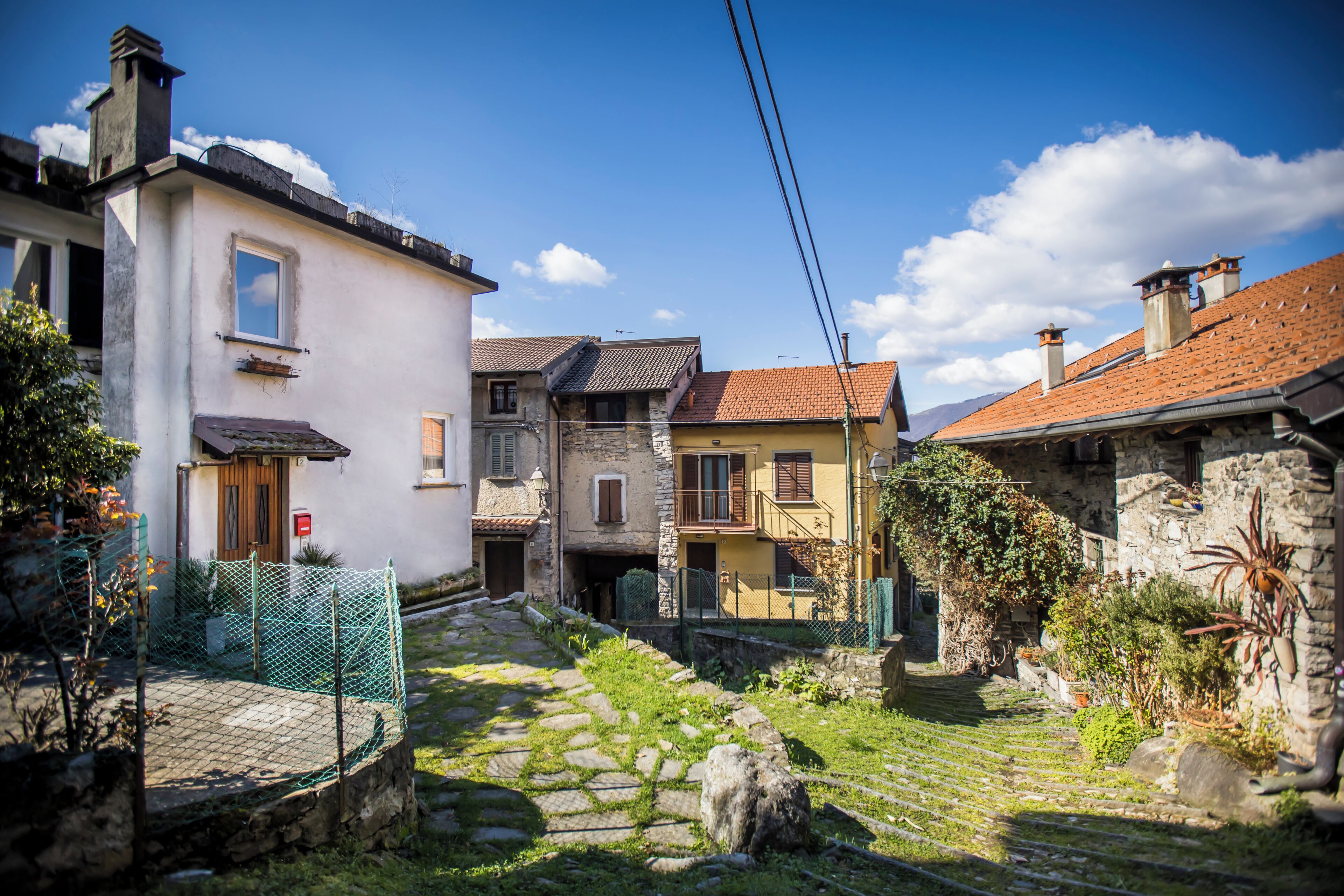 A narrow cobblestone street with traditional buildings, a stone wall, and a green fence.