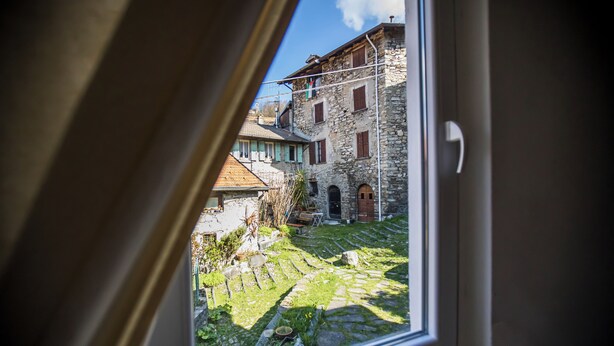 A stone building with a window, a stone wall, and a small garden area. - Casa Caramello (Palanzo)